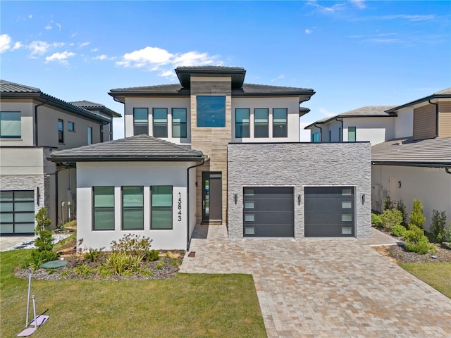 prairie-style house featuring stucco siding, a front lawn, a garage, stone siding, and decorative driveway