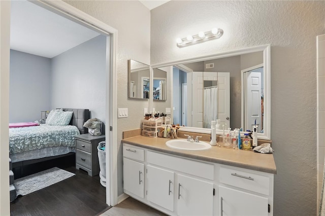 ensuite bathroom with a textured wall, wood finished floors, connected bathroom, and vanity