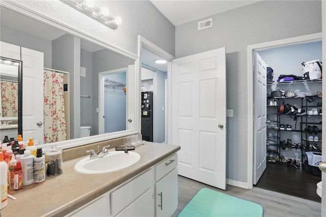 bathroom featuring a walk in closet, visible vents, toilet, vanity, and wood finished floors