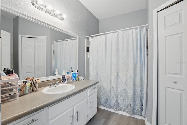 full bathroom with a shower with shower curtain, a textured wall, wood finished floors, and vanity