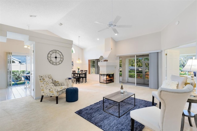 carpeted living area with visible vents, ceiling fan, a multi sided fireplace, high vaulted ceiling, and a textured ceiling