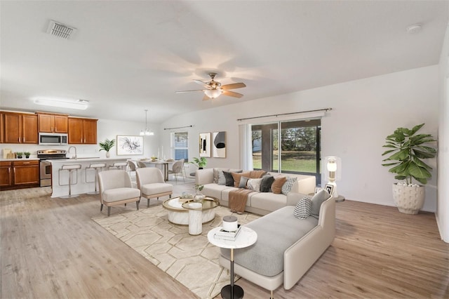 living area featuring visible vents, vaulted ceiling, light wood-style flooring, and ceiling fan with notable chandelier