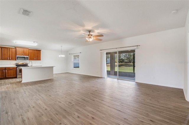 unfurnished living room with lofted ceiling, ceiling fan with notable chandelier, wood finished floors, visible vents, and baseboards