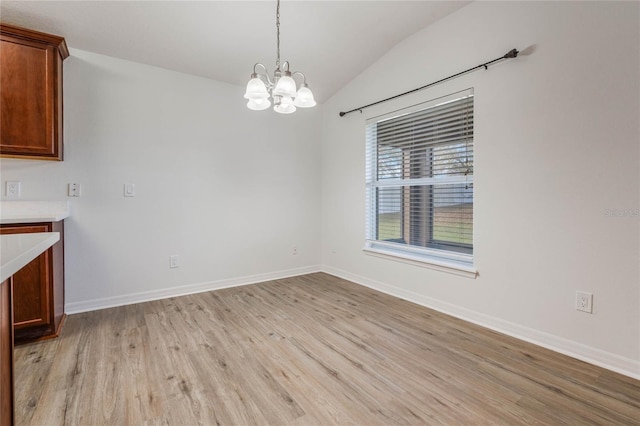 unfurnished dining area with light wood-style floors, lofted ceiling, baseboards, and an inviting chandelier