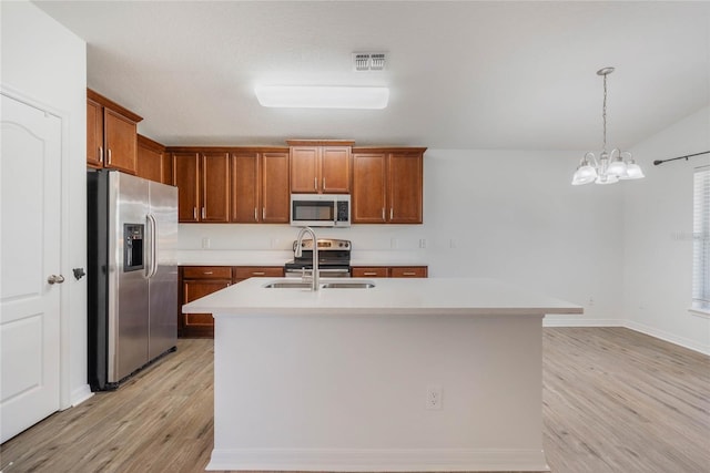 kitchen with a center island with sink, brown cabinetry, hanging light fixtures, stainless steel appliances, and light countertops