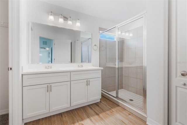 bathroom with double vanity, wood finished floors, a stall shower, and a sink