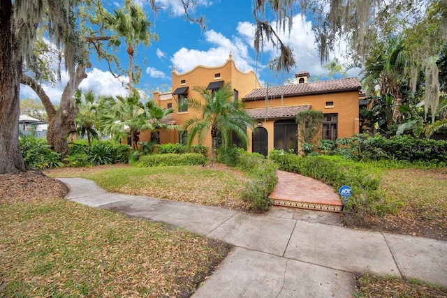 view of front facade featuring a tile roof, a front lawn, and stucco siding