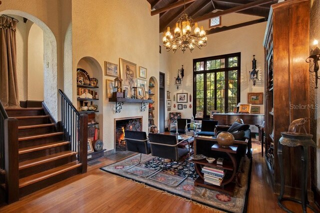 living room featuring built in features, stairs, a lit fireplace, beamed ceiling, and wood-type flooring