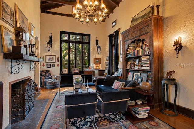 living area featuring beam ceiling, a notable chandelier, a fireplace, wood finished floors, and baseboards