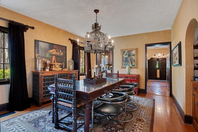 dining area with arched walkways, a notable chandelier, wood-type flooring, a textured wall, and baseboards