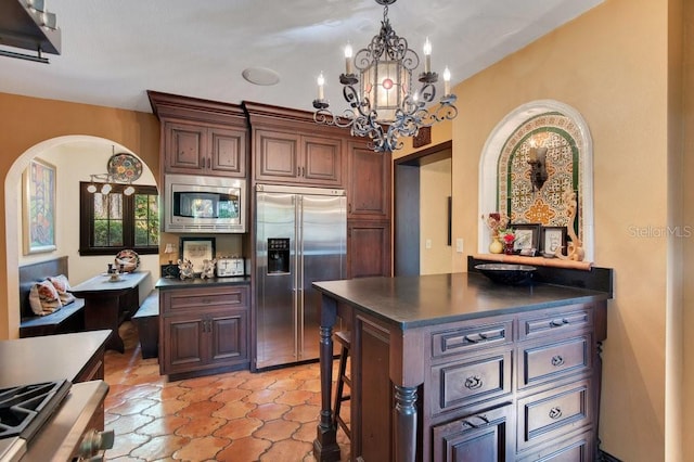 kitchen with dark countertops, hanging light fixtures, arched walkways, and built in appliances