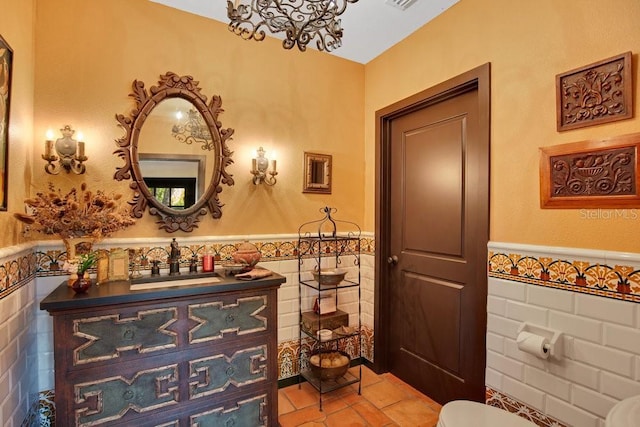 half bath featuring a wainscoted wall, toilet, vanity, and tile walls