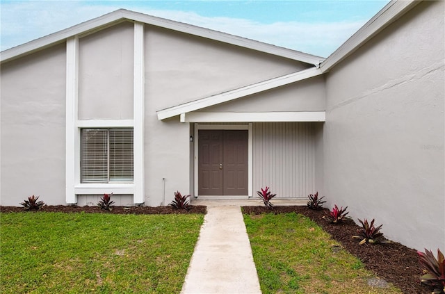 view of exterior entry with a lawn and stucco siding