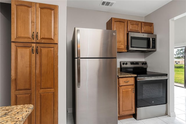 kitchen featuring appliances with stainless steel finishes, stone countertops, brown cabinetry, and visible vents