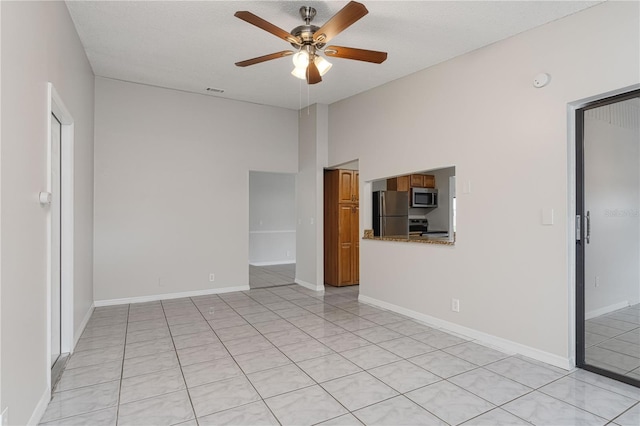 empty room featuring a ceiling fan, light tile patterned flooring, visible vents, and baseboards