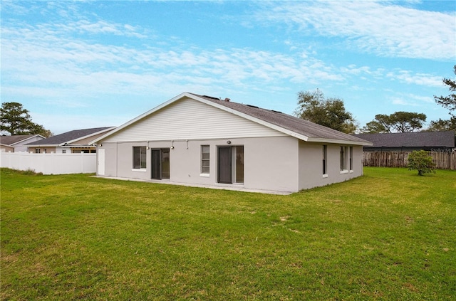 rear view of property featuring a lawn, fence, and stucco siding