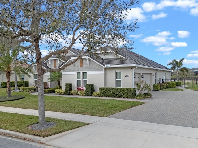 view of front of house with an attached garage, fence, decorative driveway, a front lawn, and stucco siding