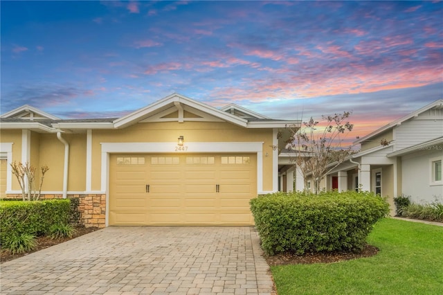 view of front facade featuring stone siding, decorative driveway, an attached garage, and stucco siding