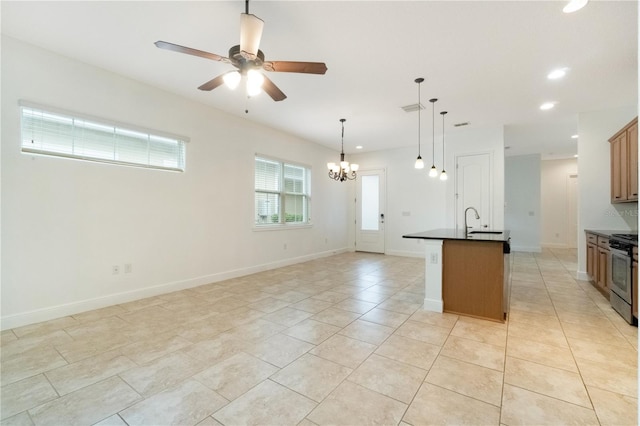 kitchen with stainless steel range, dark countertops, an island with sink, brown cabinets, and a sink