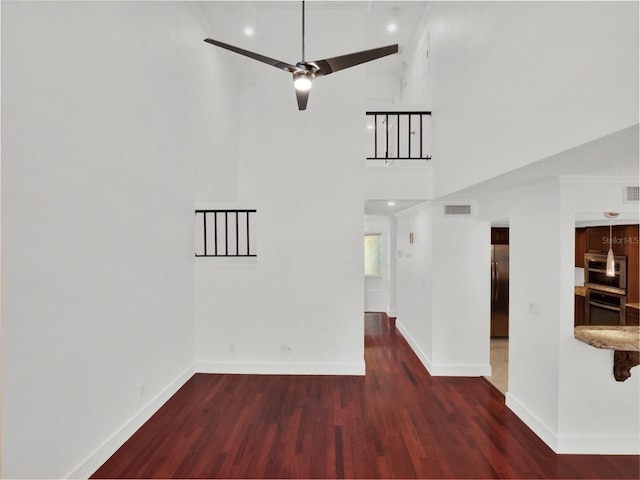 unfurnished room featuring dark wood-style flooring, a towering ceiling, baseboards, visible vents, and a ceiling fan