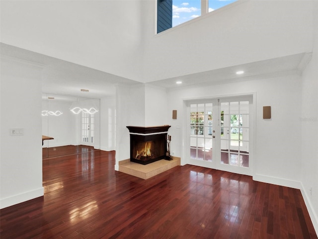 unfurnished living room featuring a lit fireplace, french doors, dark wood-style flooring, and baseboards