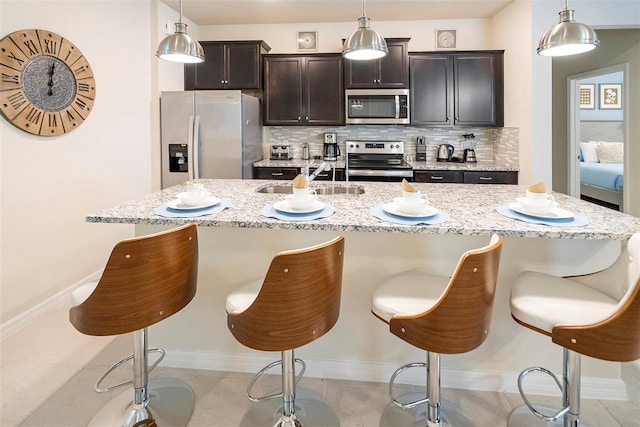 kitchen featuring appliances with stainless steel finishes, a breakfast bar, a kitchen island with sink, and decorative light fixtures