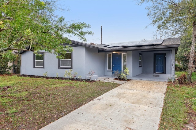 single story home with covered porch, stucco siding, a front lawn, and solar panels