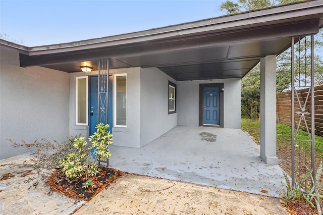 view of exterior entry with fence and stucco siding