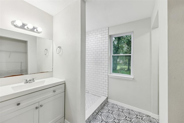 bathroom featuring tiled shower, vanity, baseboards, and tile patterned floors