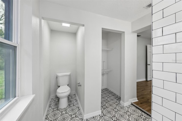 bathroom featuring visible vents, baseboards, toilet, tile patterned flooring, and a textured ceiling