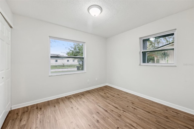 empty room featuring a textured ceiling, light wood-style flooring, and baseboards