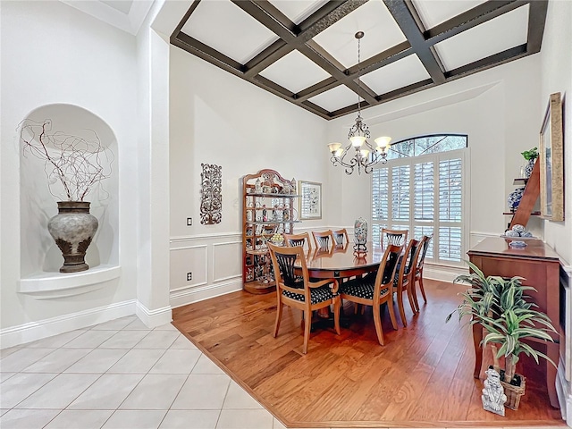 dining room with light wood-style floors, a chandelier, coffered ceiling, and beam ceiling