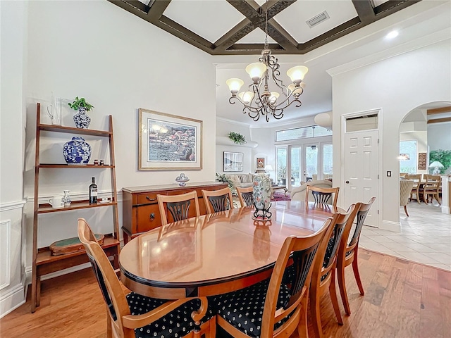 dining room with arched walkways, light wood-style flooring, a high ceiling, coffered ceiling, and visible vents