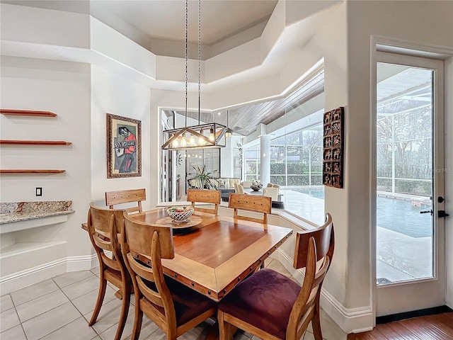 dining space featuring a tray ceiling, an inviting chandelier, baseboards, and light tile patterned floors