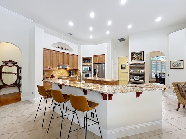 kitchen featuring light tile patterned floors, arched walkways, a spacious island, stainless steel appliances, and backsplash