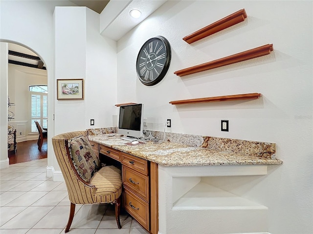 office featuring arched walkways, light tile patterned floors, built in study area, and baseboards