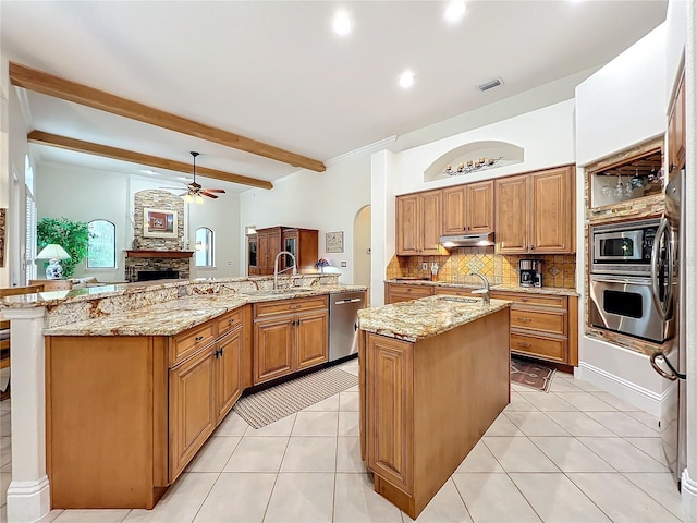 kitchen featuring arched walkways, under cabinet range hood, stainless steel appliances, a sink, and an island with sink