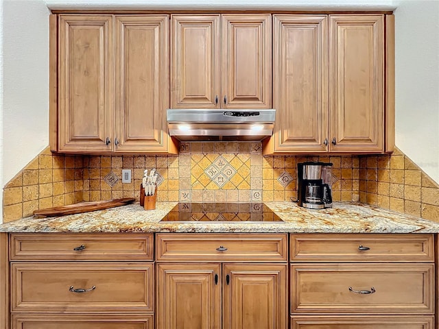 kitchen featuring light stone countertops, decorative backsplash, black electric cooktop, and under cabinet range hood