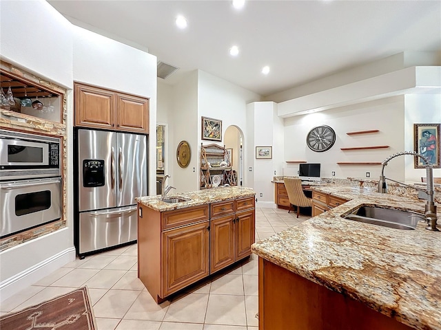 kitchen featuring light tile patterned floors, arched walkways, stainless steel appliances, a sink, and an island with sink