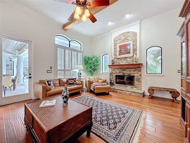 living room featuring hardwood / wood-style flooring, ceiling fan, ornamental molding, beamed ceiling, and a stone fireplace