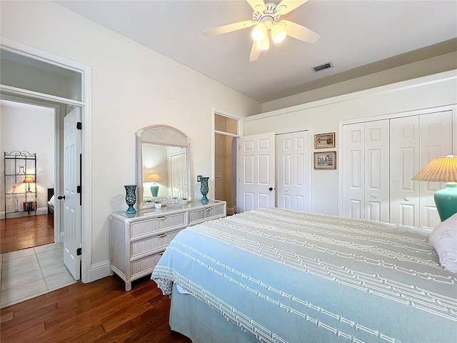 bedroom with dark wood-style floors, a ceiling fan, visible vents, and multiple closets