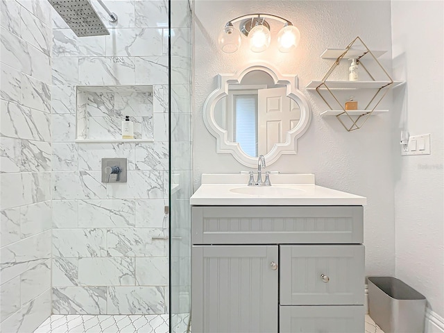 bathroom featuring tiled shower, a textured wall, and vanity