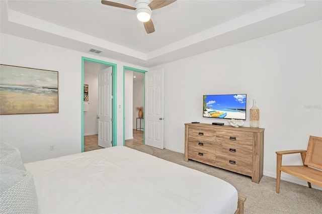 bedroom with a ceiling fan, a tray ceiling, light carpet, and visible vents