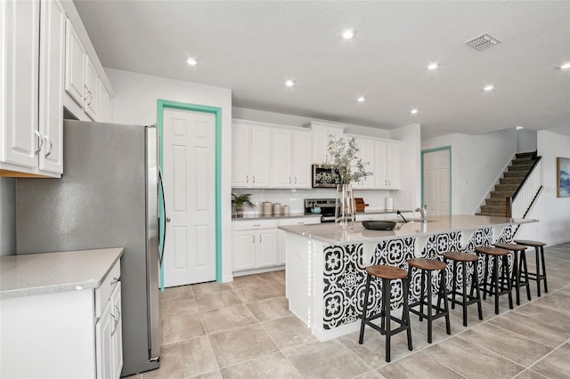 kitchen featuring visible vents, white cabinets, light countertops, appliances with stainless steel finishes, and an island with sink