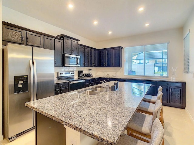 kitchen featuring a center island with sink, light stone counters, a breakfast bar, stainless steel appliances, and a sink