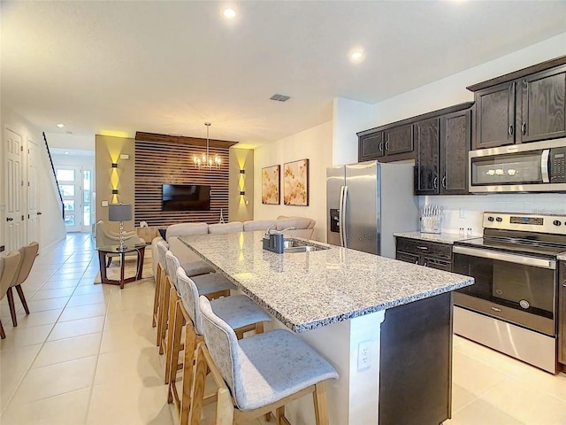 kitchen featuring appliances with stainless steel finishes, open floor plan, a kitchen island with sink, light stone countertops, and a kitchen bar