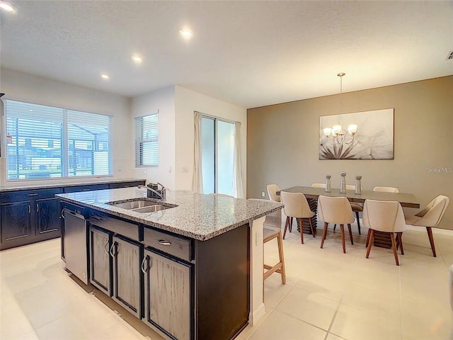 kitchen featuring light stone counters, decorative light fixtures, a sink, and an island with sink