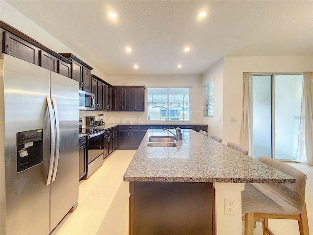 kitchen featuring light stone counters, a breakfast bar, appliances with stainless steel finishes, a kitchen island with sink, and a sink