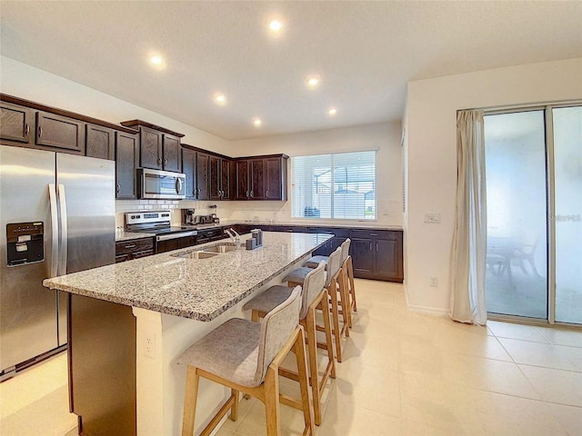 kitchen featuring light stone counters, a breakfast bar area, a kitchen island with sink, appliances with stainless steel finishes, and decorative backsplash