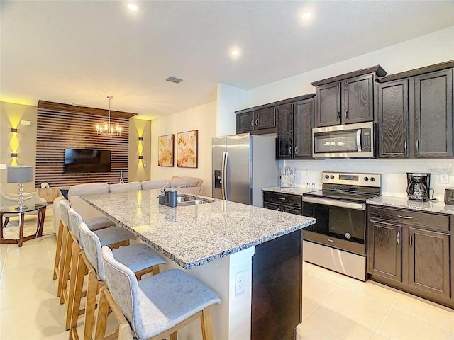 kitchen featuring appliances with stainless steel finishes, open floor plan, light stone counters, a kitchen island with sink, and a kitchen bar